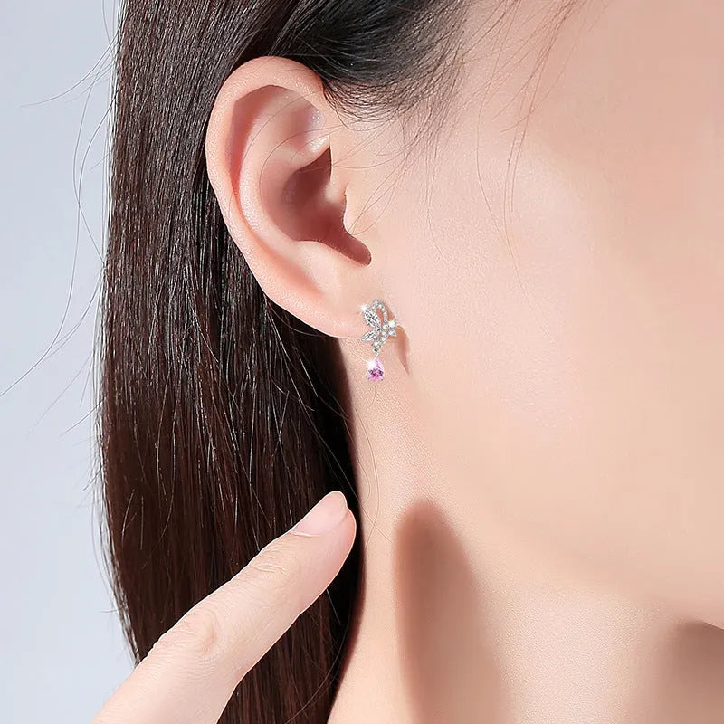 Close-up of a pair of silver butterfly stud earrings on a plain background.