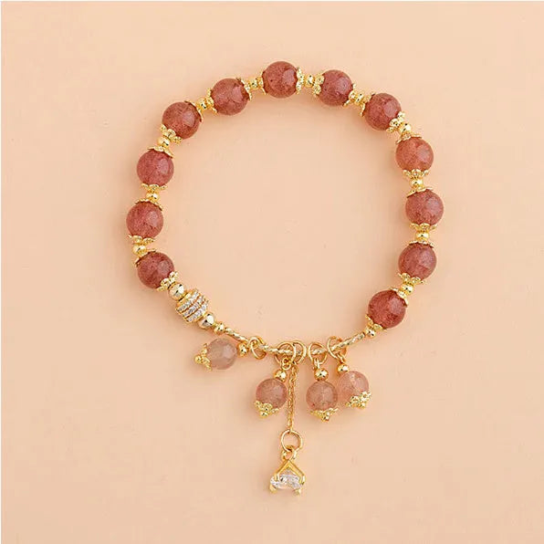 Close-up of a pink heart-shaped strawberry quartz crystal bracelet with pearl details on a wrist.