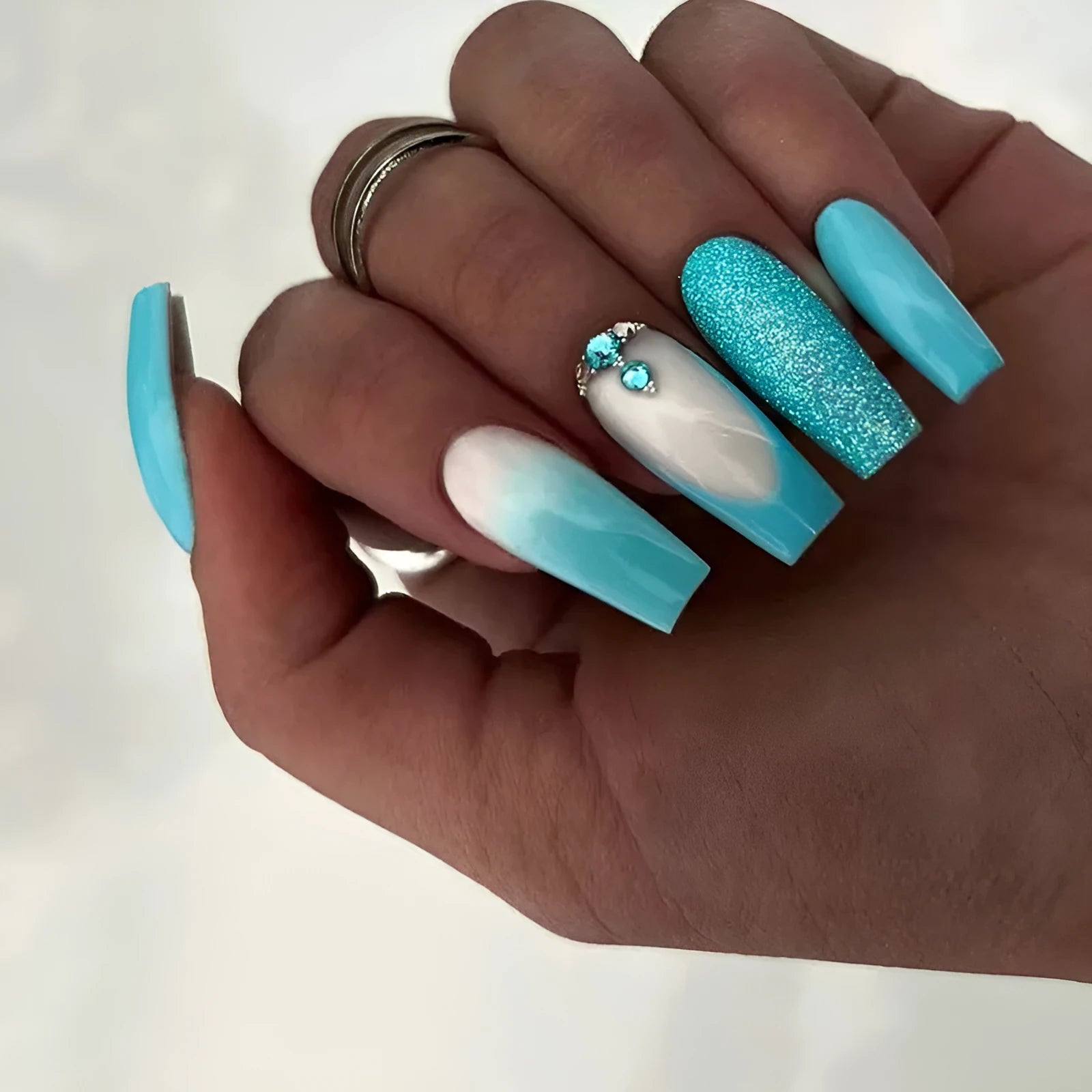 Long ballet false nails with blue diamond glitter on solid colour background with nail glue bottle