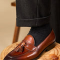Men's black polished leather tassel loafers on a white background, side view showing rubber sole.