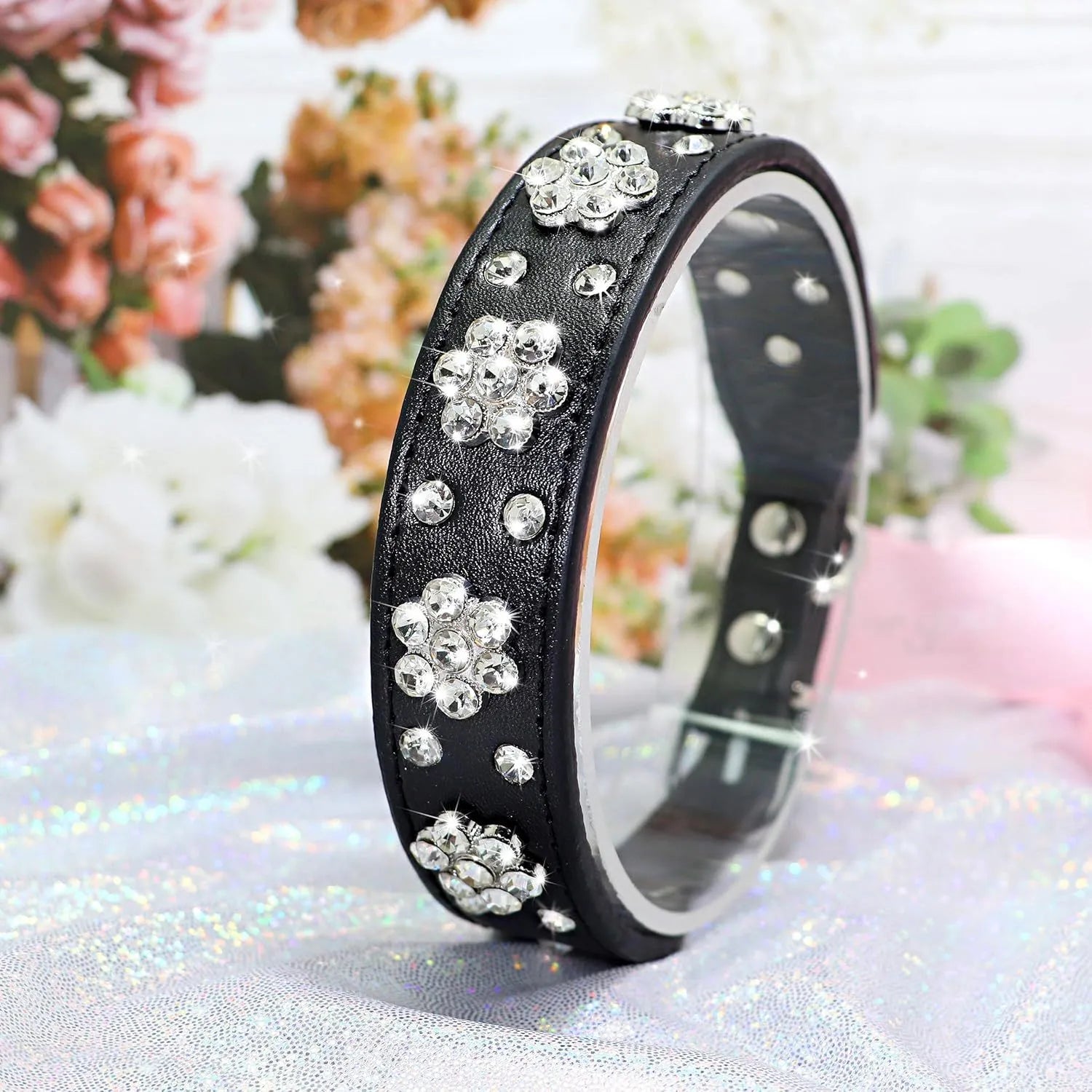 Close-up of a black PU leather dog collar with silver rhinestone flowers and studs, showing the metal D-ring.