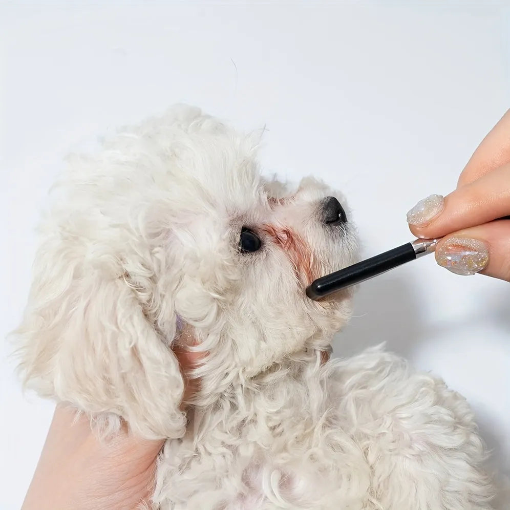 Black handheld pet grooming brush with a soft silicone head for eye tear stain removal.