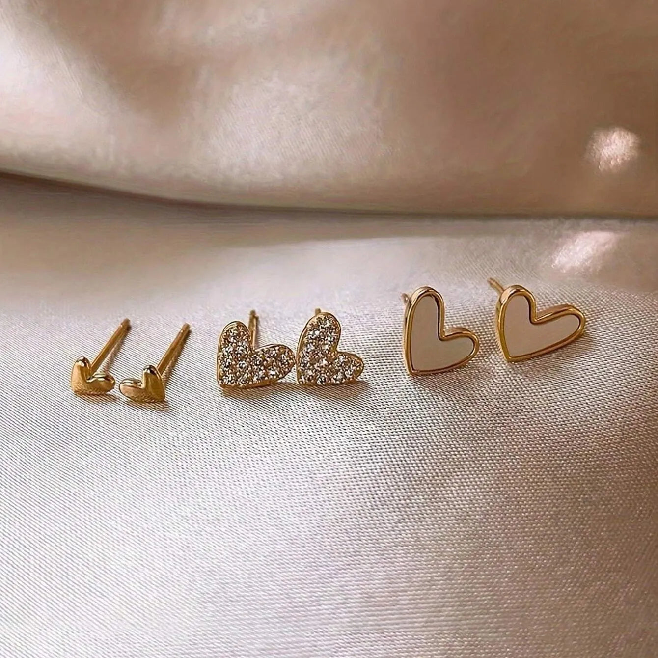 Three pairs of heart-shaped alloy earrings in gold, black, white and pink colours