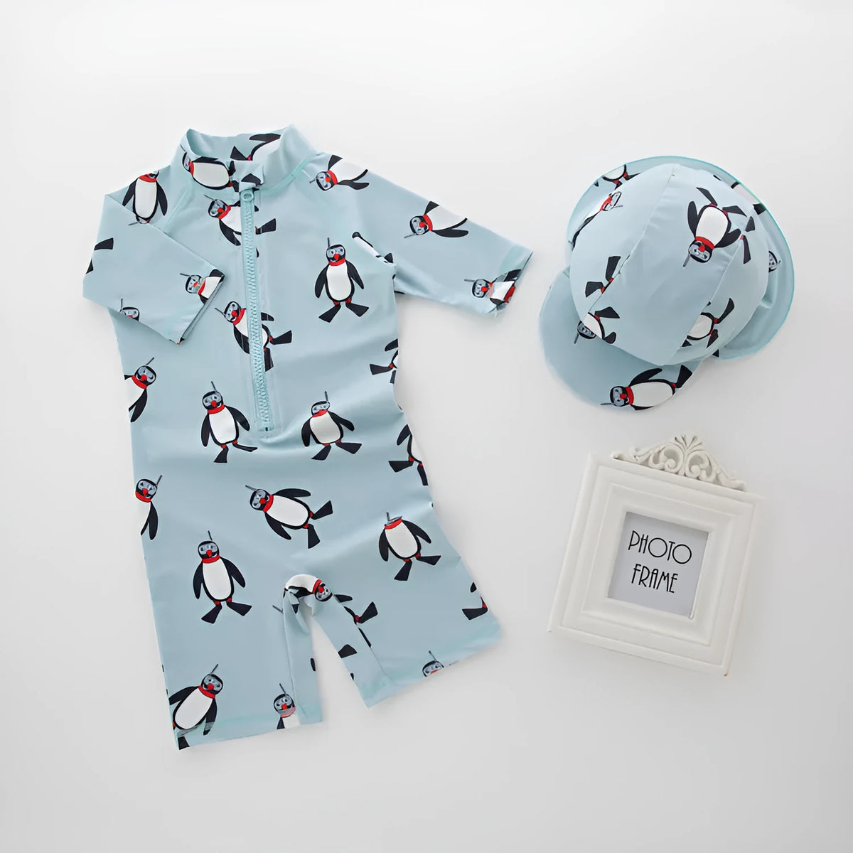 Boy's long sleeve penguin print swimsuit set with matching swimming cap on a white background.