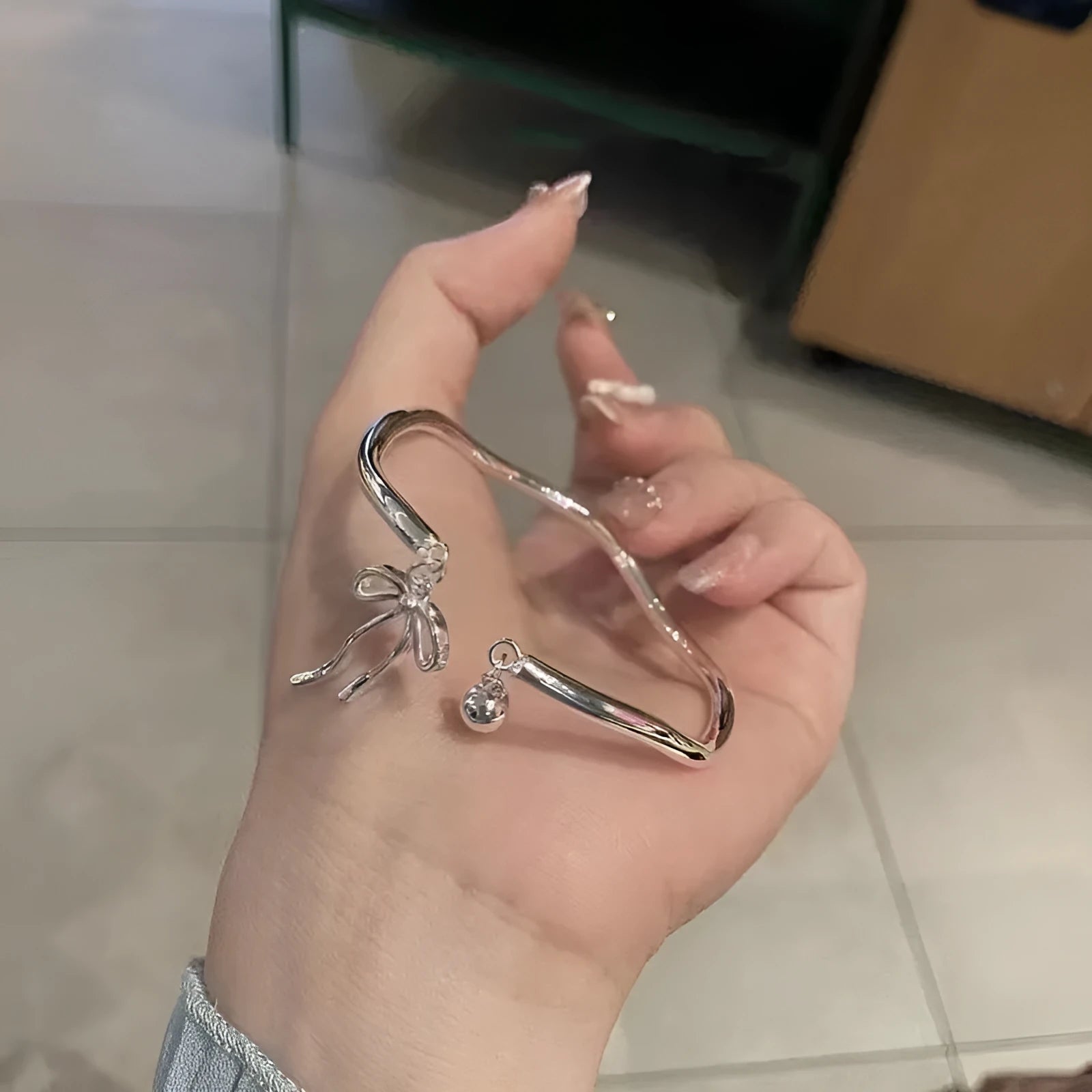 Silver bow adjustable bracelet with bell opening mechanism on wrist