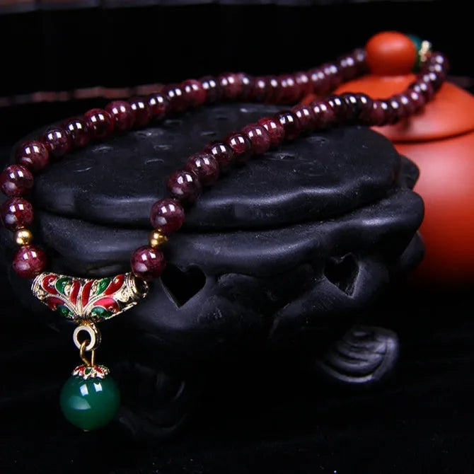 Close-up of a natural red garnet bead bracelet with a golden toad charm on a wrist.