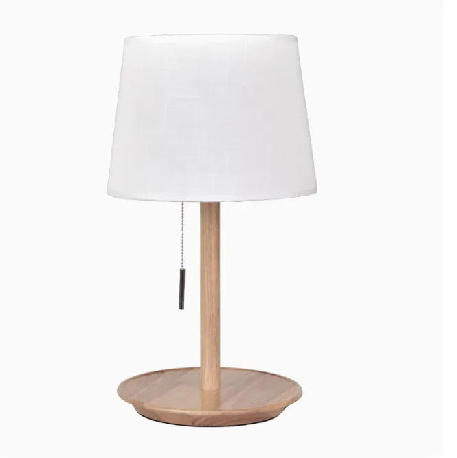 Walnut coloured solid wood bedside lamp with white cloth shade on a table.