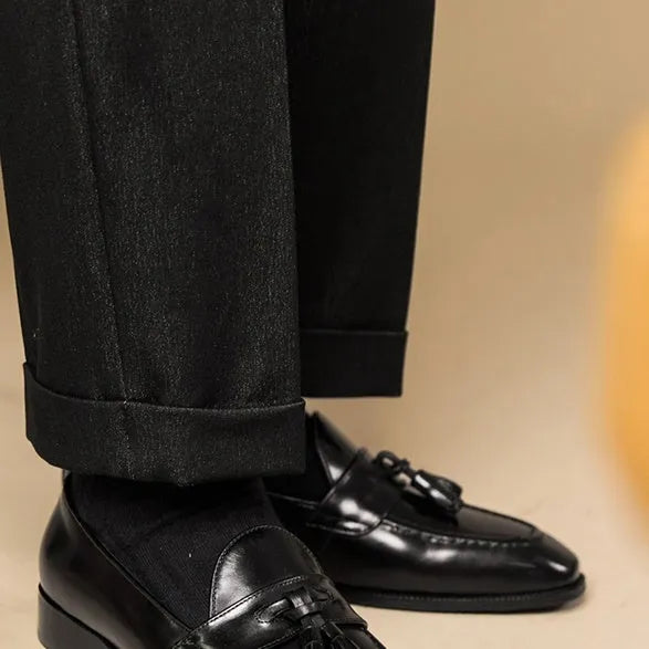 Men's black polished leather tassel loafers on a white background, side view showing rubber sole.