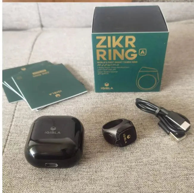 Zikr1 smart ring in silver showing OLED display with Tasbih count, next to charging case.