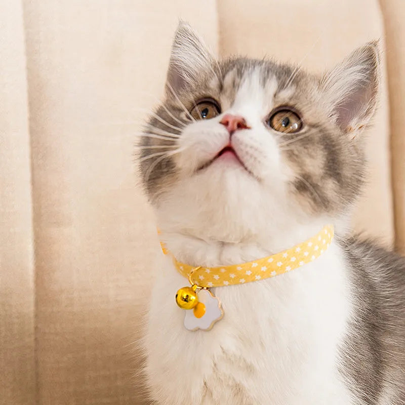 Green adjustable cat collar with a small bell and bow tie pendant on a white background.