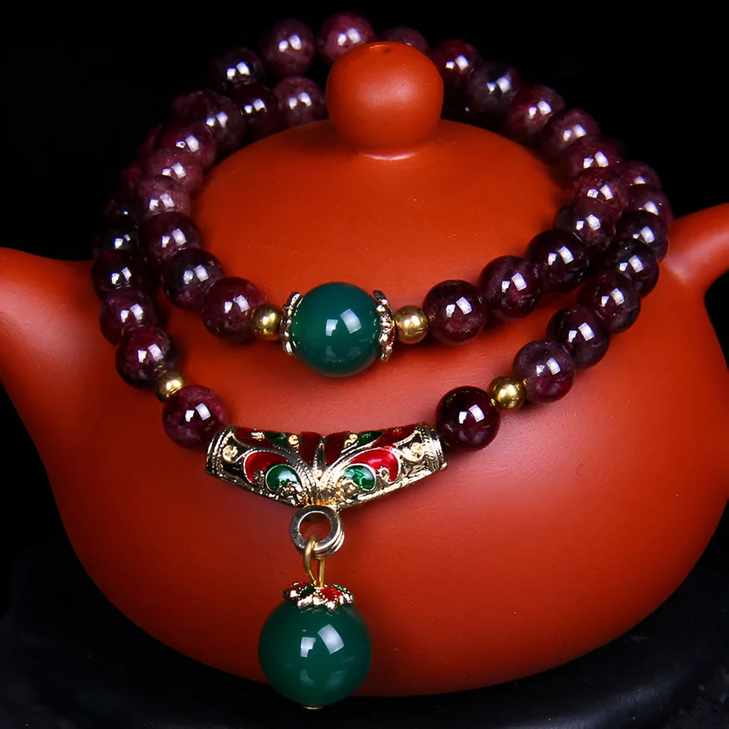 Close-up of a natural red garnet bead bracelet with a golden toad charm on a wrist.
