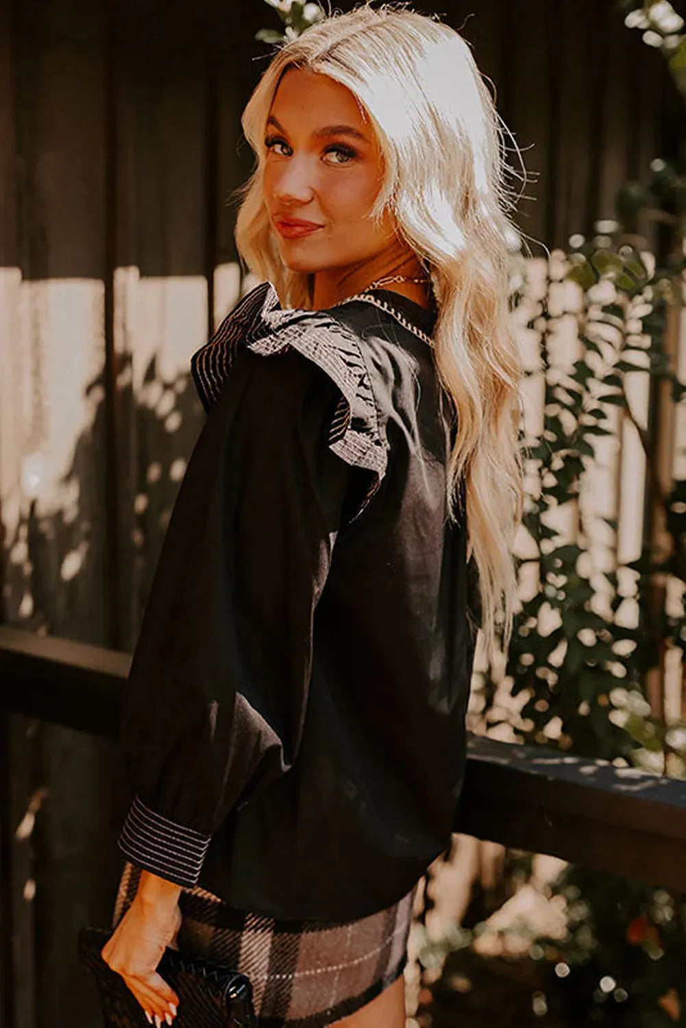 Black V-neck long sleeve blouse with ruffle detail and contrast stitching.