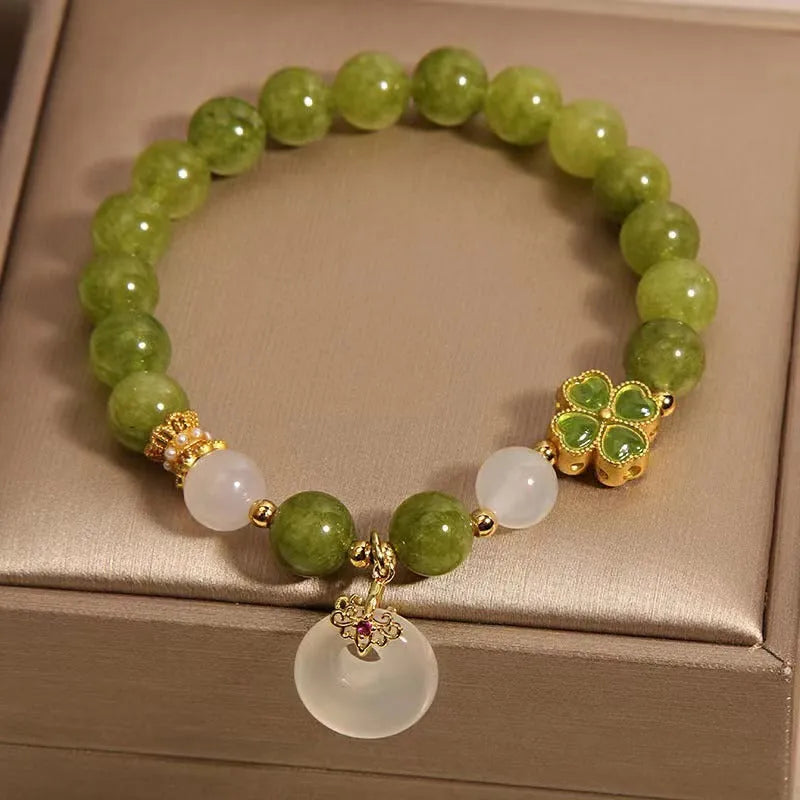 Women's green tourmaline bracelet with four-leaf clover safety buckle on a wrist.