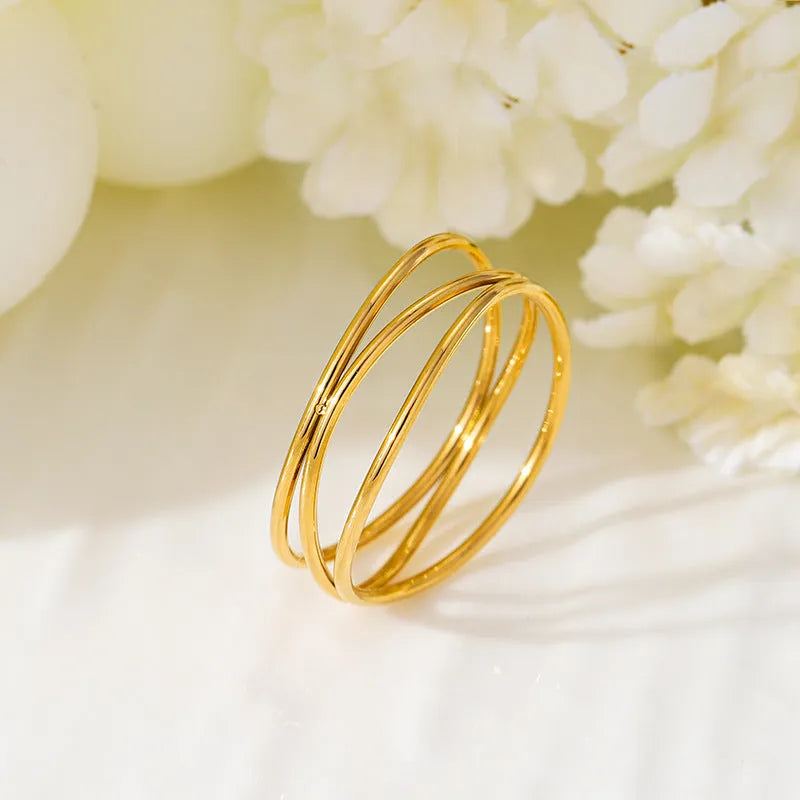 Gold-coloured titanium steel geometric ring with a three-layer coil design on a plain background.