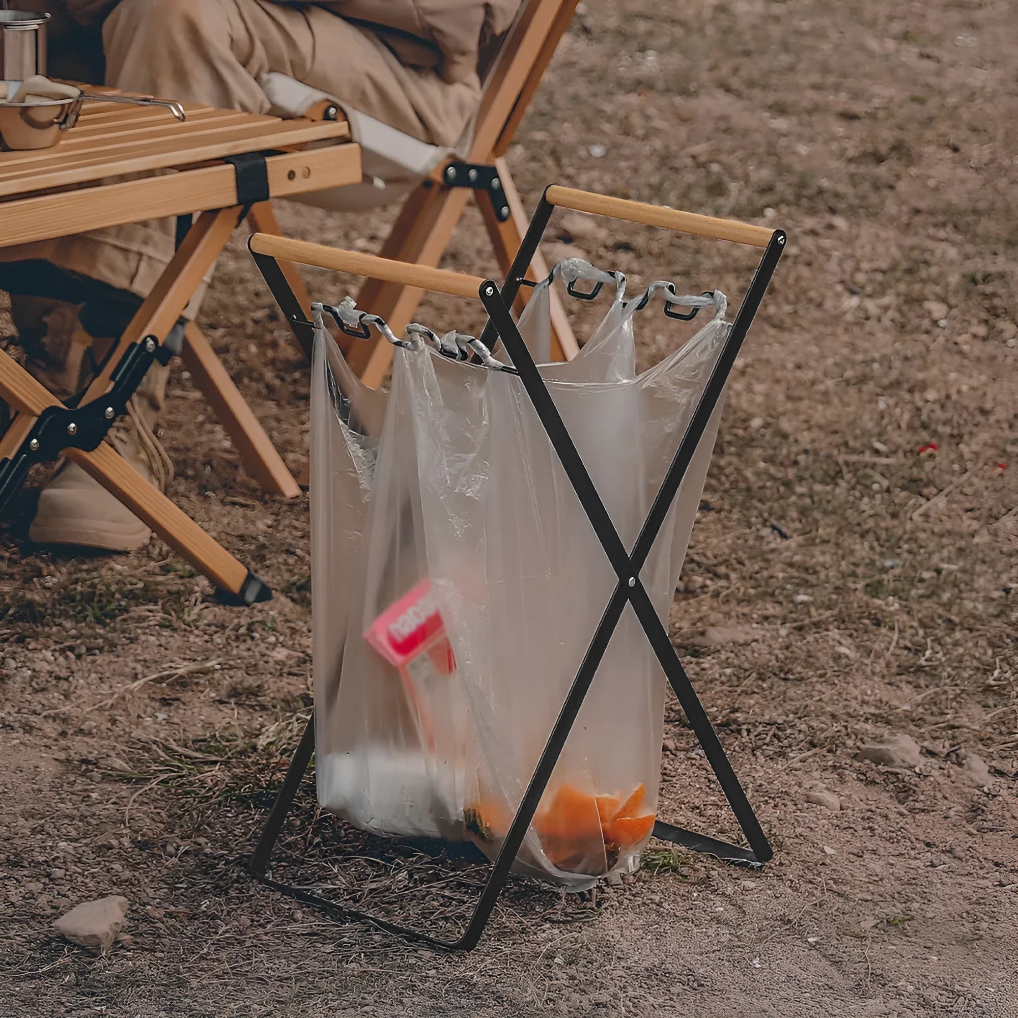 Black foldable iron trash storage hanger with wooden handle holding a bin bag outdoors.