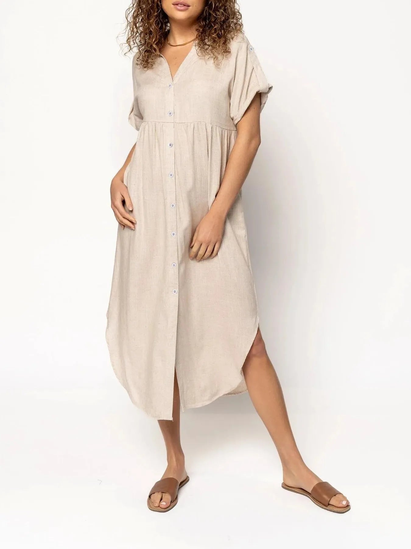A woman wearing a loose-fitting, mid-length apricot-coloured casual dress with a button-down front.