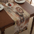 Dark blue striped table runner with jacquard bouquet pattern and tassel ends on a wooden table.