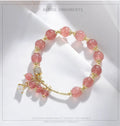 Close-up of a pink heart-shaped strawberry quartz crystal bracelet with pearl details on a wrist.