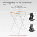Black foldable iron trash storage hanger with wooden handle holding a bin bag outdoors.