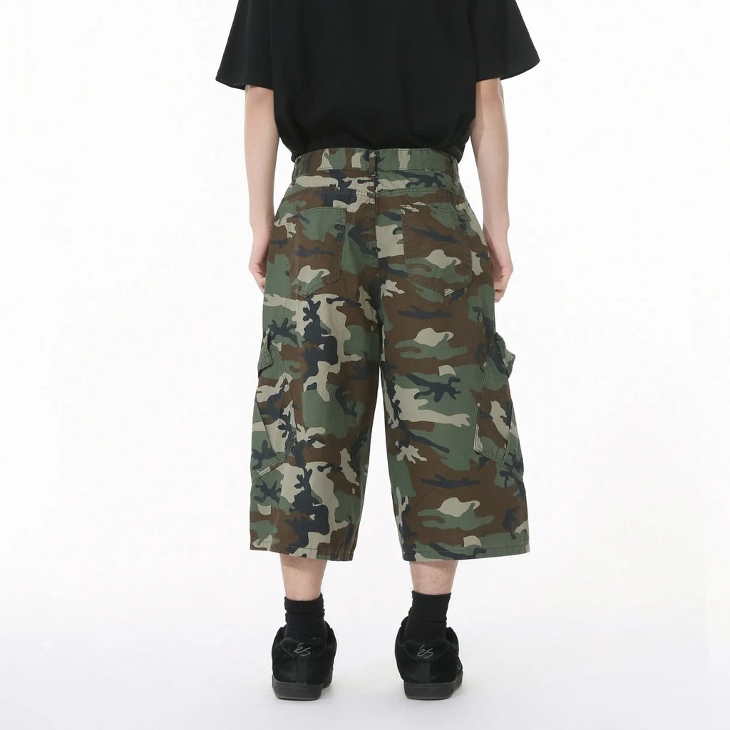 Men's loose-fit camouflage cotton trousers with wide legs, cropped hem, side stitching, and large front pockets.