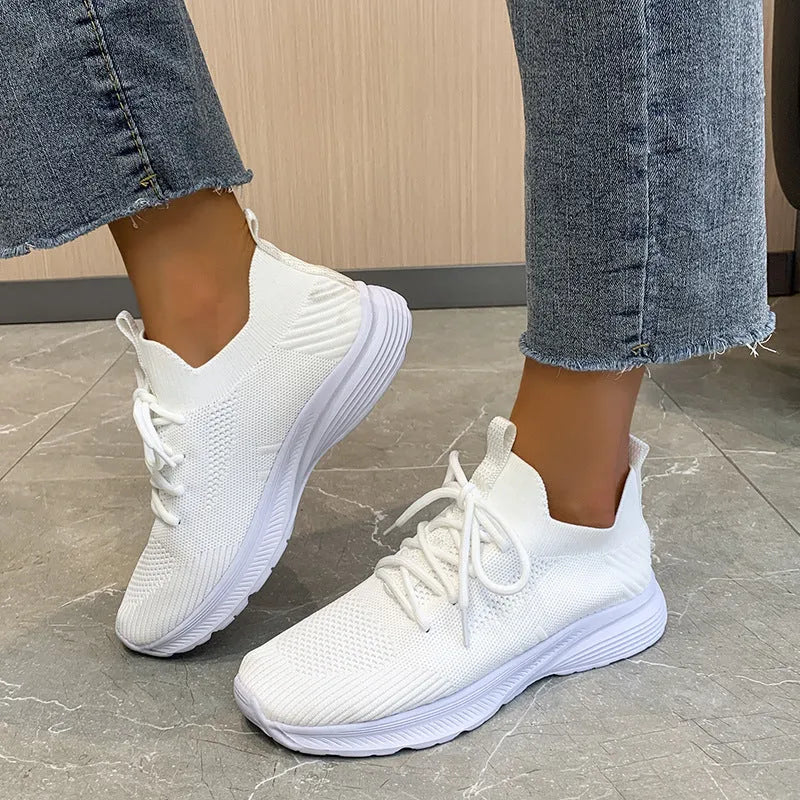 Women's creamy white low-top running shoes with a Flyknit upper and mesh detailing on a flat rubber sole.