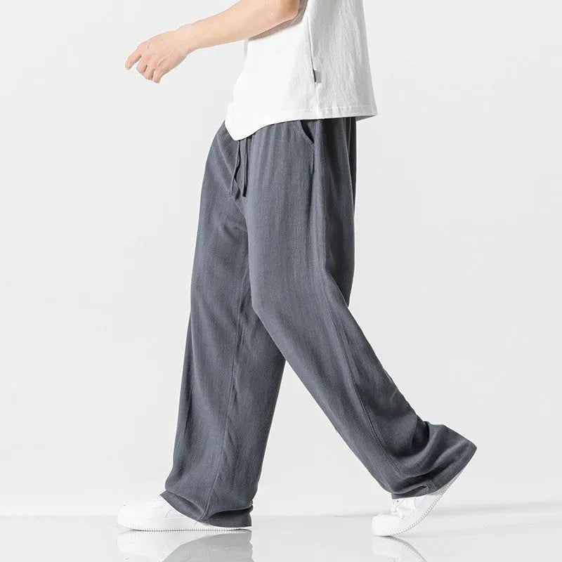 Men's beige loose-fit straight-leg linen trousers with drawstring waist, shown on a model.
