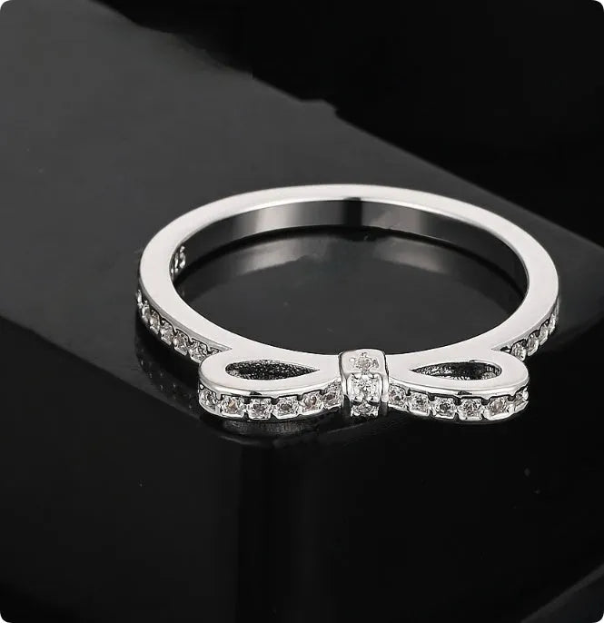 Silver-coloured bow-shaped ring with clear rhinestone embellishments on a white background