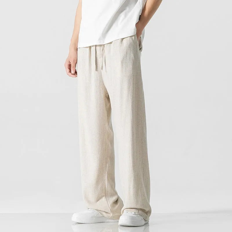 Men's beige loose-fit straight-leg linen trousers with drawstring waist, shown on a model.