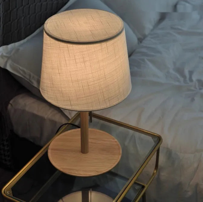 Walnut coloured solid wood bedside lamp with white cloth shade on a table.