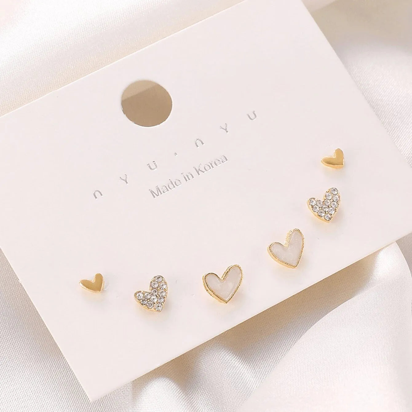 Three pairs of heart-shaped alloy earrings in gold, black, white and pink colours