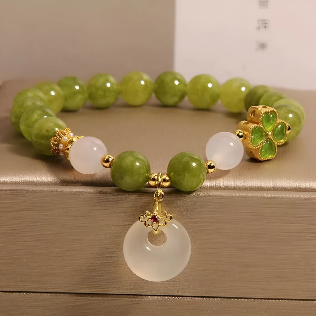 Women's green tourmaline bracelet with four-leaf clover safety buckle on a wrist.