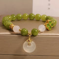 Women's green tourmaline bracelet with four-leaf clover safety buckle on a wrist.