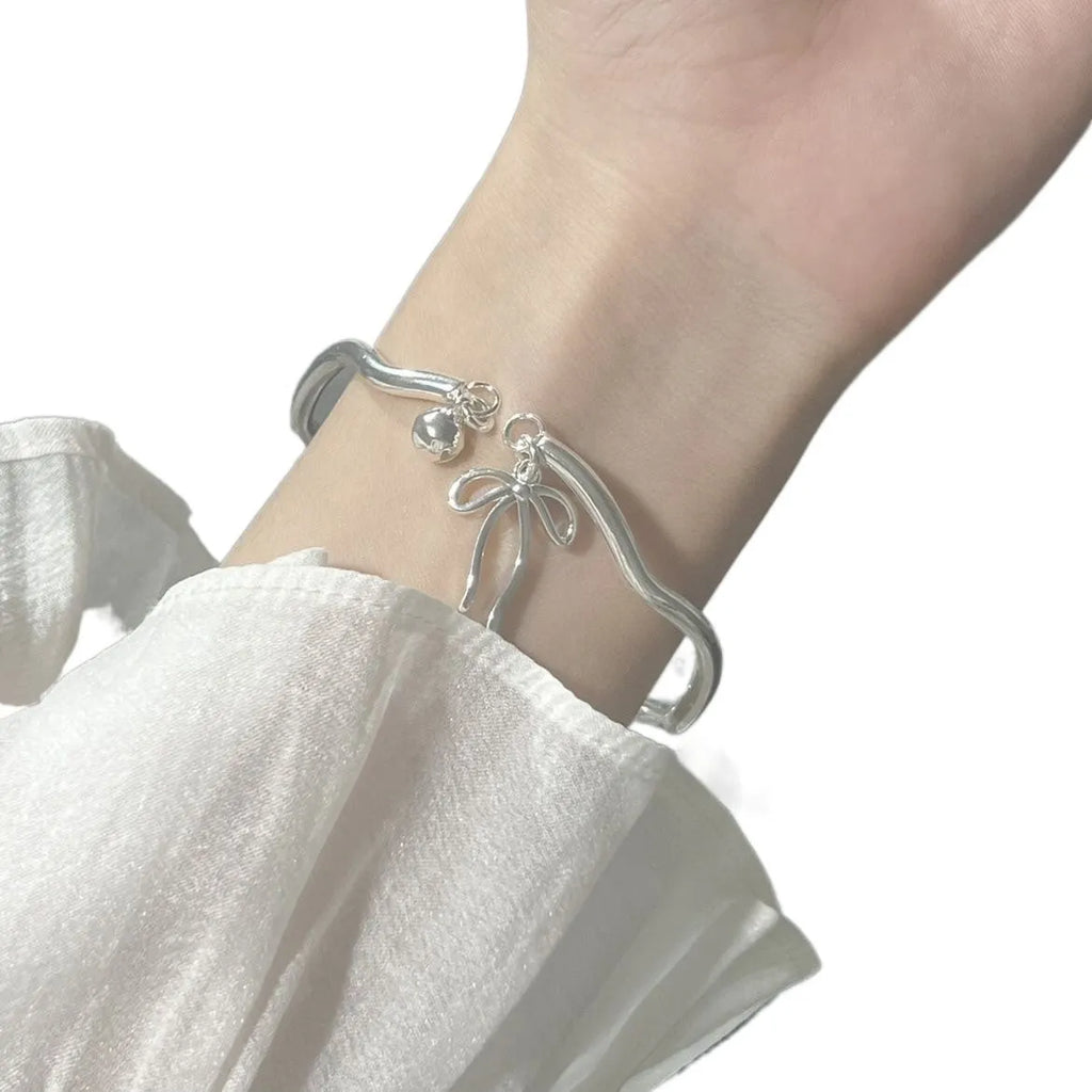 Silver bow adjustable bracelet with bell opening mechanism on wrist