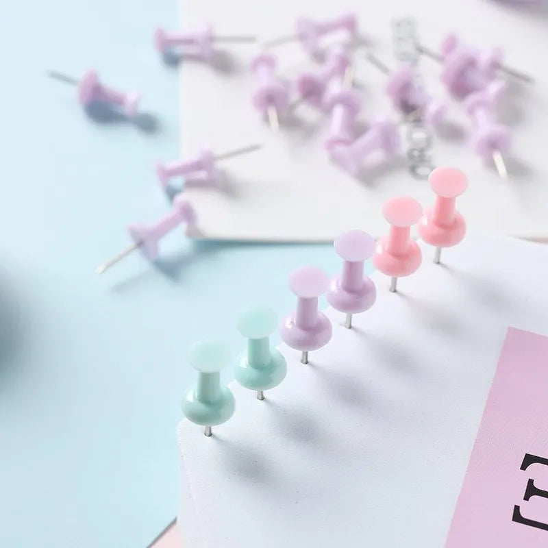 Box of coloured plastic push pins in cherry blossom pink, mint green and lavender on a white surface